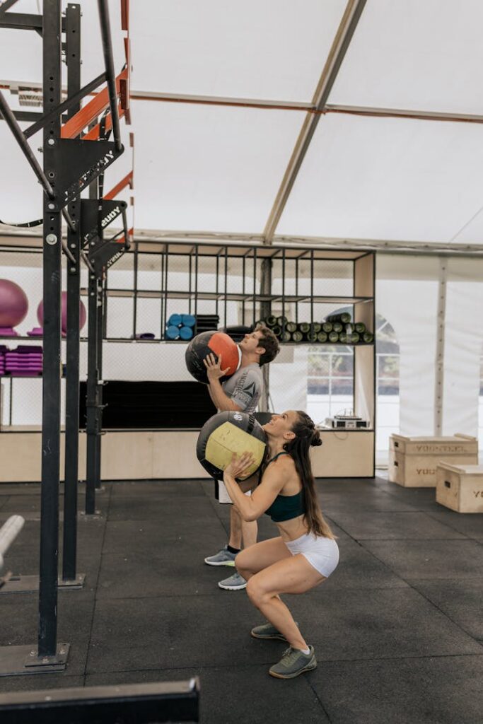 A man and woman working out with medicine balls in an indoor gym setting.